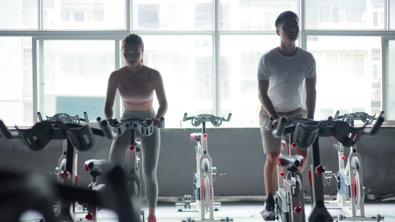 亚洲女人和男人在健身房进行自行车训练视频下载