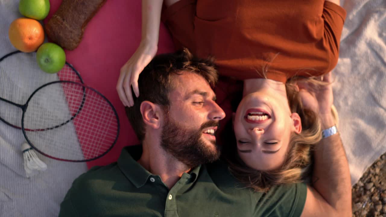 幸福的年轻夫妇，躺在野餐毯上，分享彼此的深情，庆祝他们的爱情视频下载