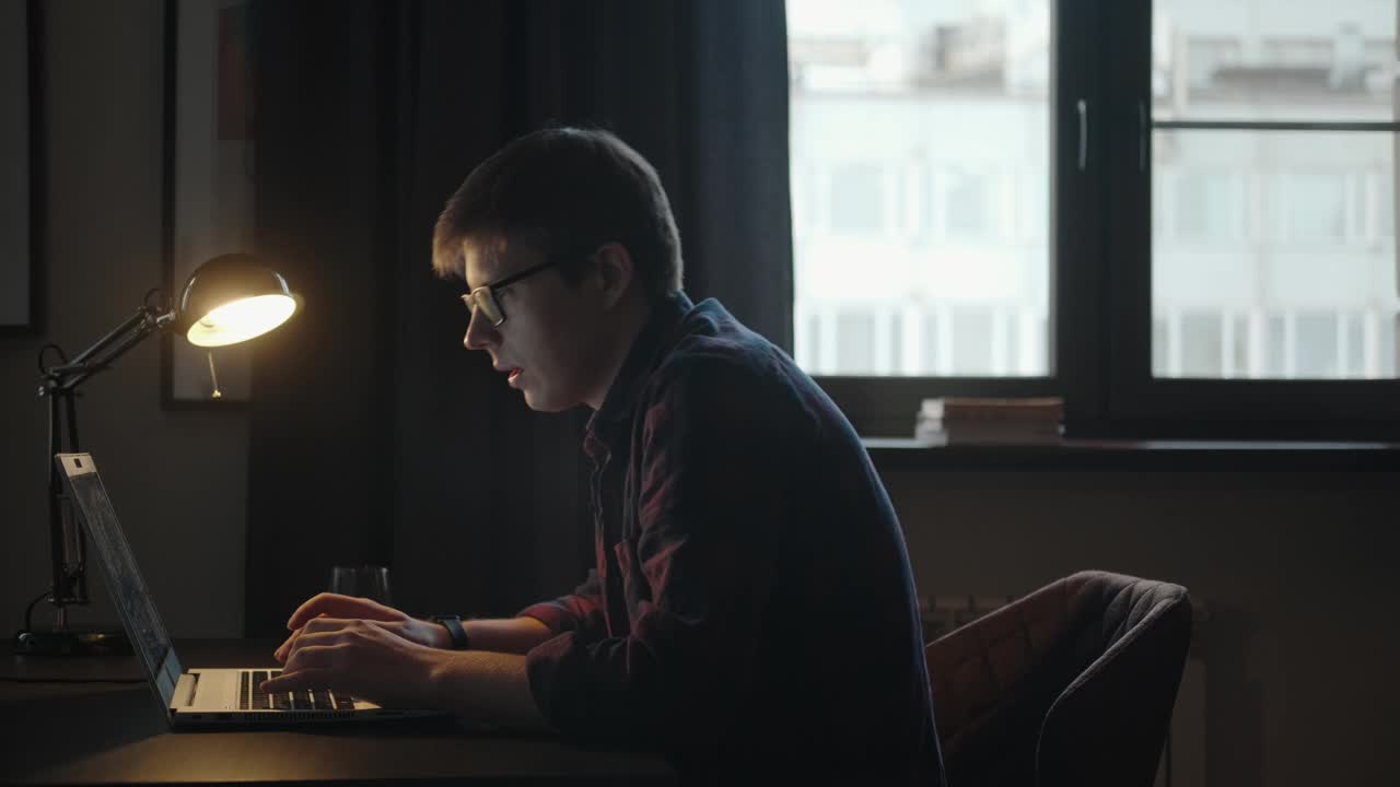 自由职业者在家里的一个房间里工作。一个男人坐在桌子旁，手里拿着一台笔记本电脑视频下载