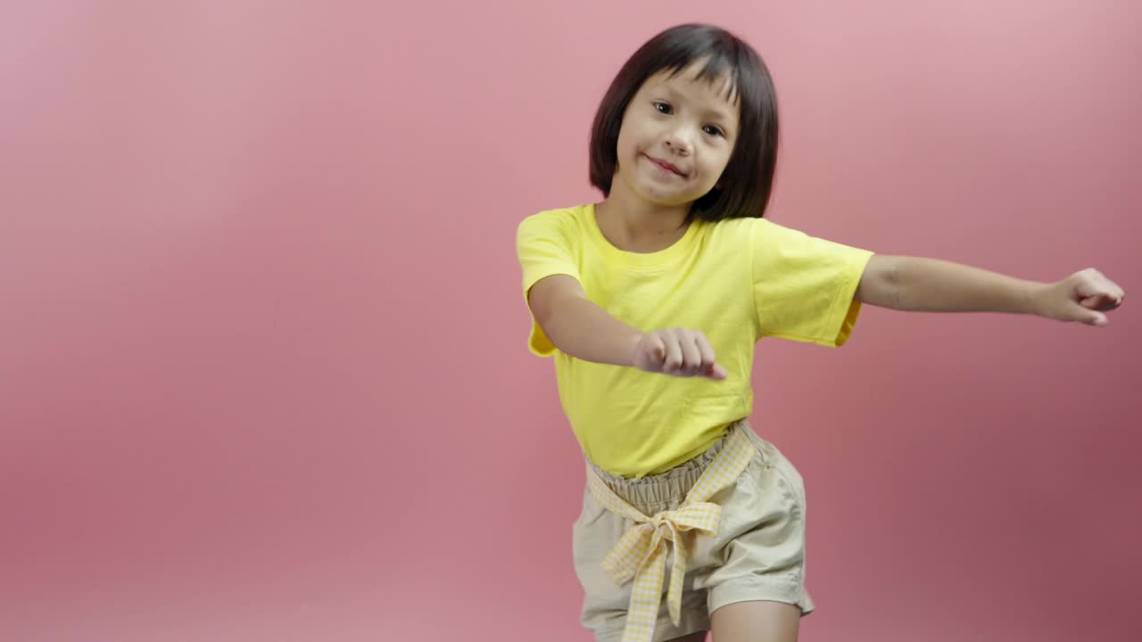 小女孩听着音乐，在粉红色的背景上跳舞。视频下载