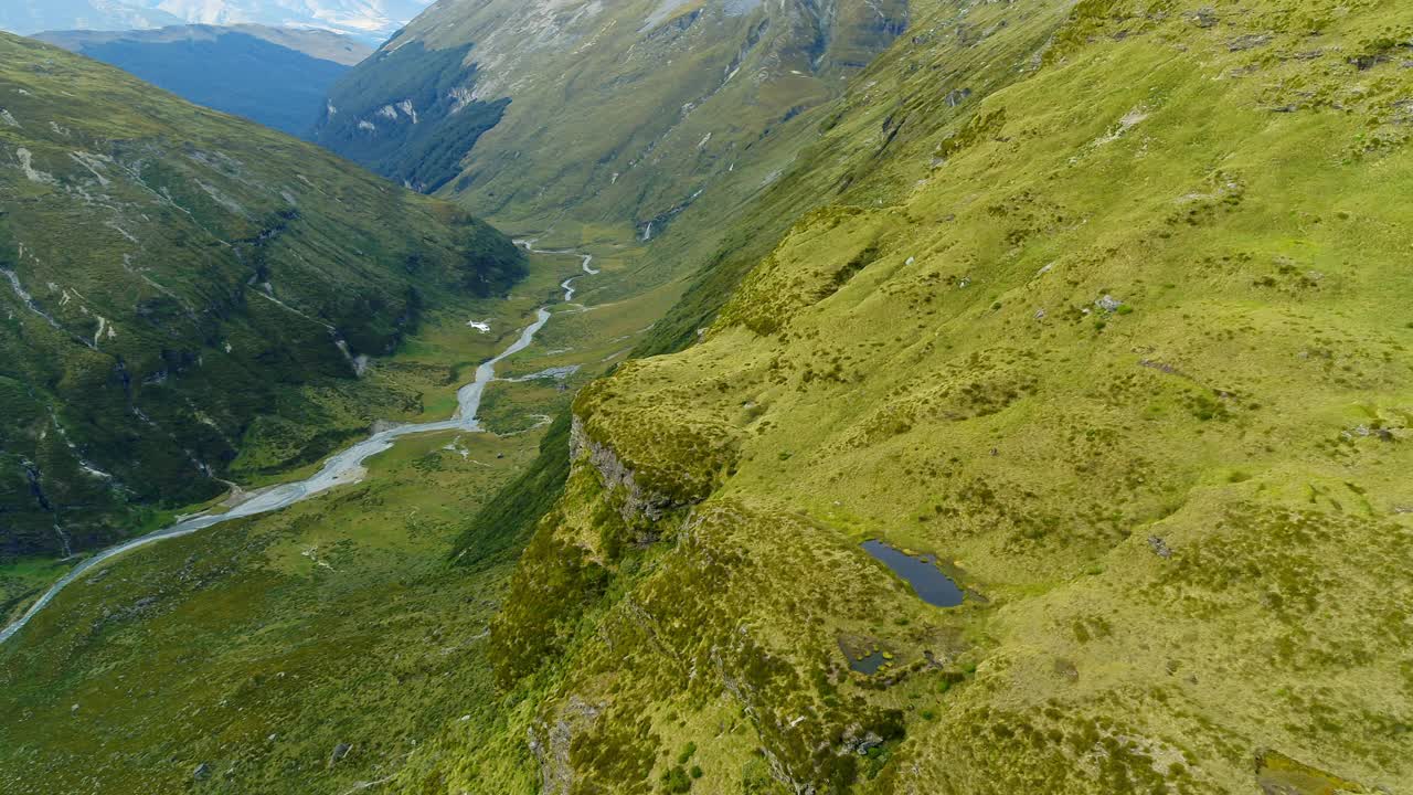 航拍:直升机飞过绿色山脉的美丽镜头，河流在景观中流动-奥克兰，新西兰视频购买