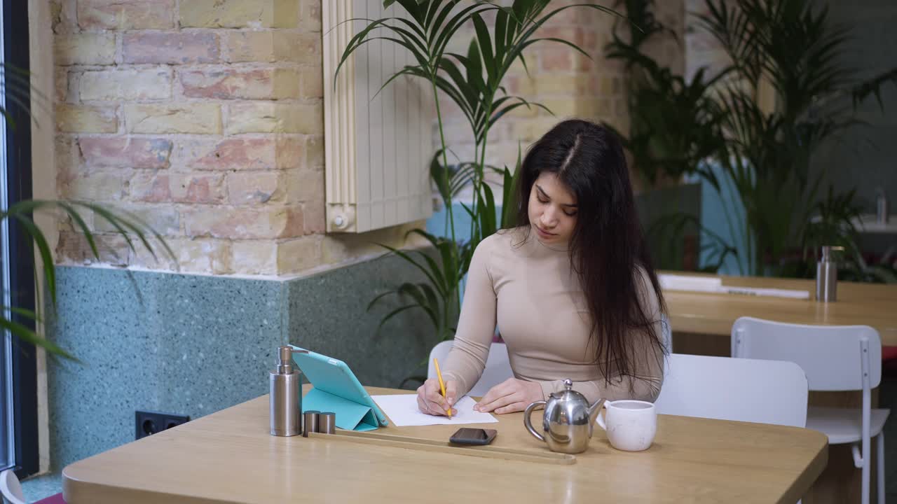 一个聪明的中东自信的年轻女商人的肖像，坐在咖啡馆里用笔记本电脑上网。美丽苗条聪明的自由职业者在餐厅在线工作。缓慢的运动。视频素材