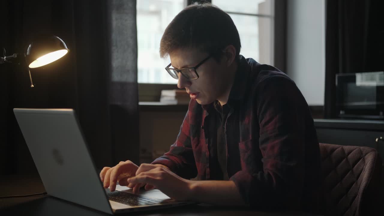 工作中的男人:在一间黑屋子里，一个年轻人坐在笔记本电脑前。视频下载