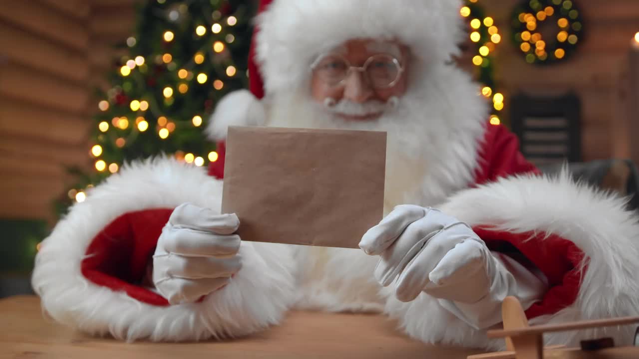 在一个装饰精美的室内，圣诞老人手持一个干净的信封，在镜头中竖起大拇指，面带亲切的微笑视频下载