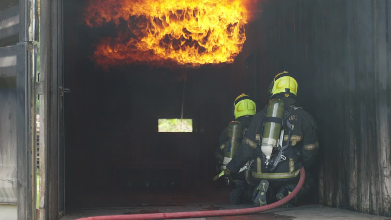 消防队员用消防水龙带灭火大楼大火。消防队员身穿消防服，头戴消防头盔，准备向被烧毁的房屋内的救援人员喷水。视频素材