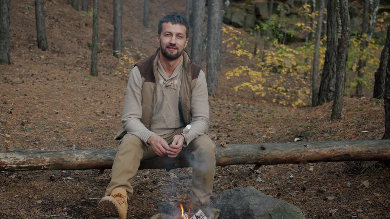 慢动作人像帅哥游客坐在篝火在森林里拿着烤棉花糖视频素材