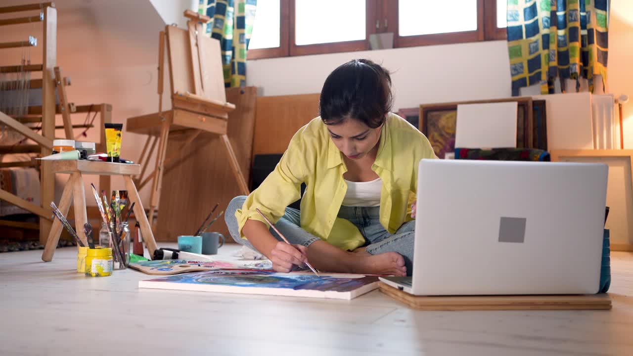 为了提高她的绘画技能，女性艺术家在她的笔记本电脑上观看在线绘画教程视频下载