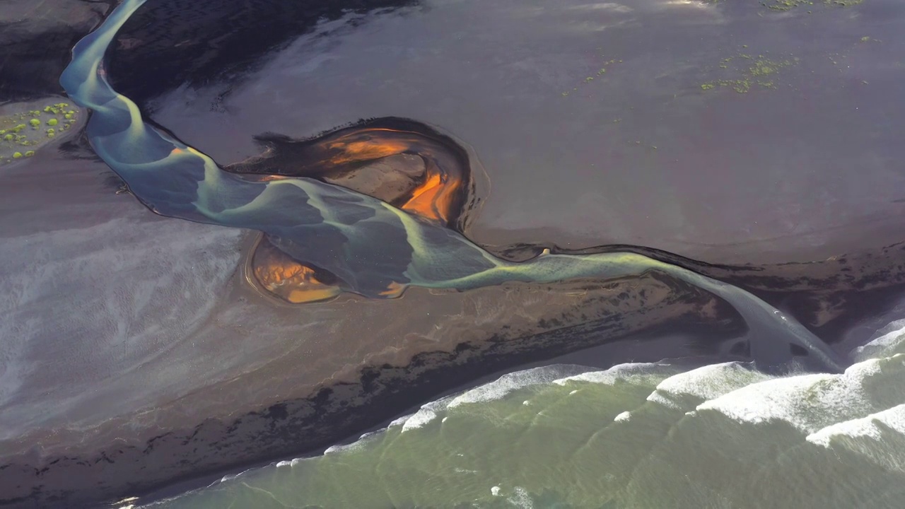 航拍视频显示，一条辫状河流过冰岛的黑色沙滩，流入大海视频素材