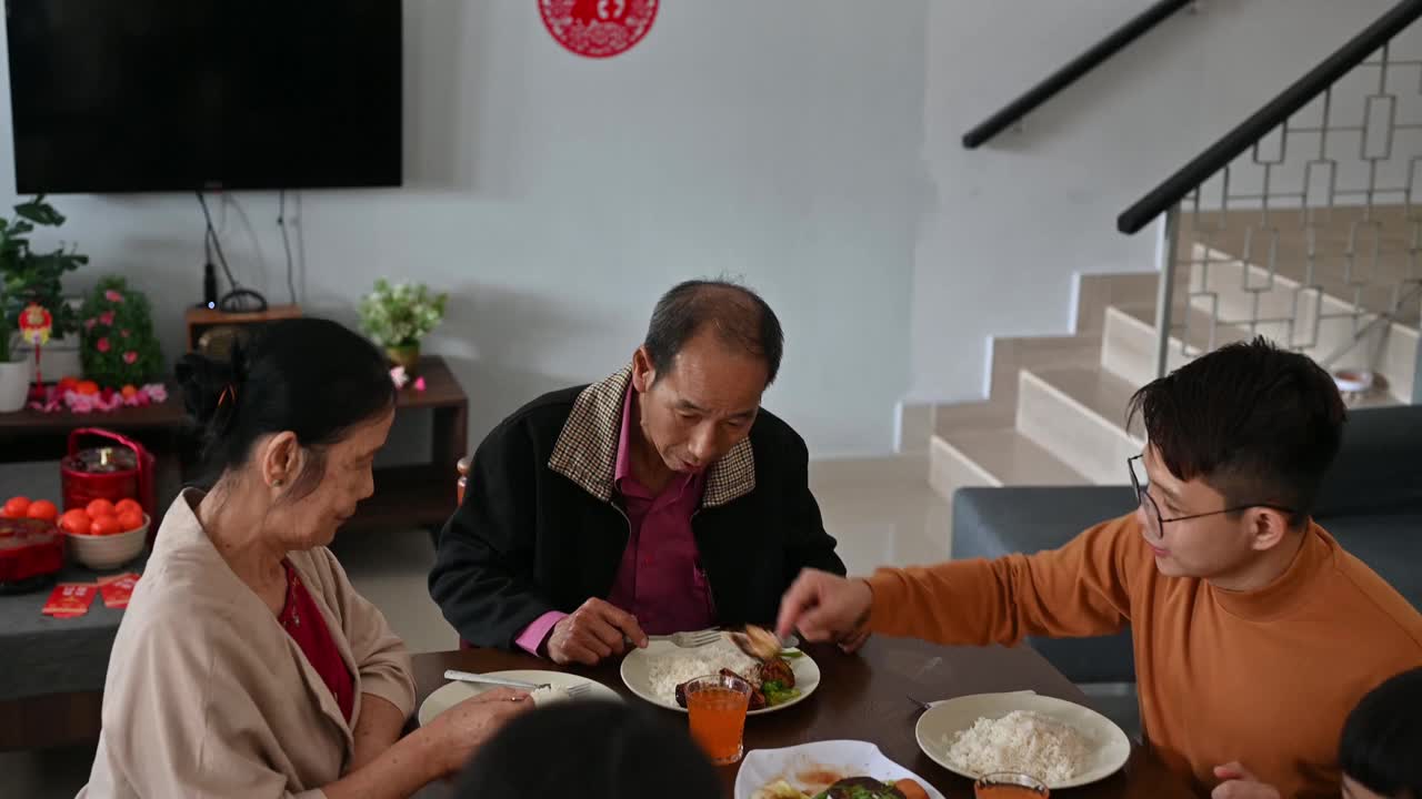 中国新年期间，一名亚洲男子在家享受团圆饭，并与母亲分享食物视频下载