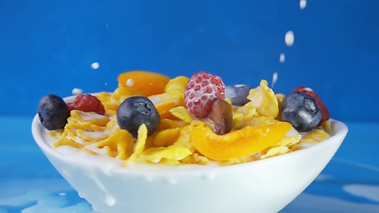 牛奶被倒进黄色的玉米片里，配上各种新鲜浆果，如蓝莓、覆盆子、葡萄和杏仁。原始慢动作速度斜坡视频。视频素材