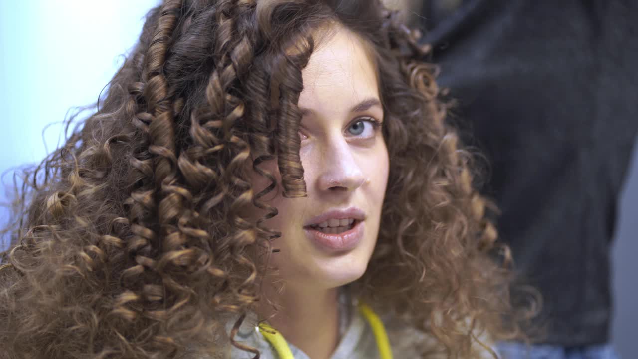 一个年轻的卷发女人正在做头发的特写，她看着镜头说话视频下载