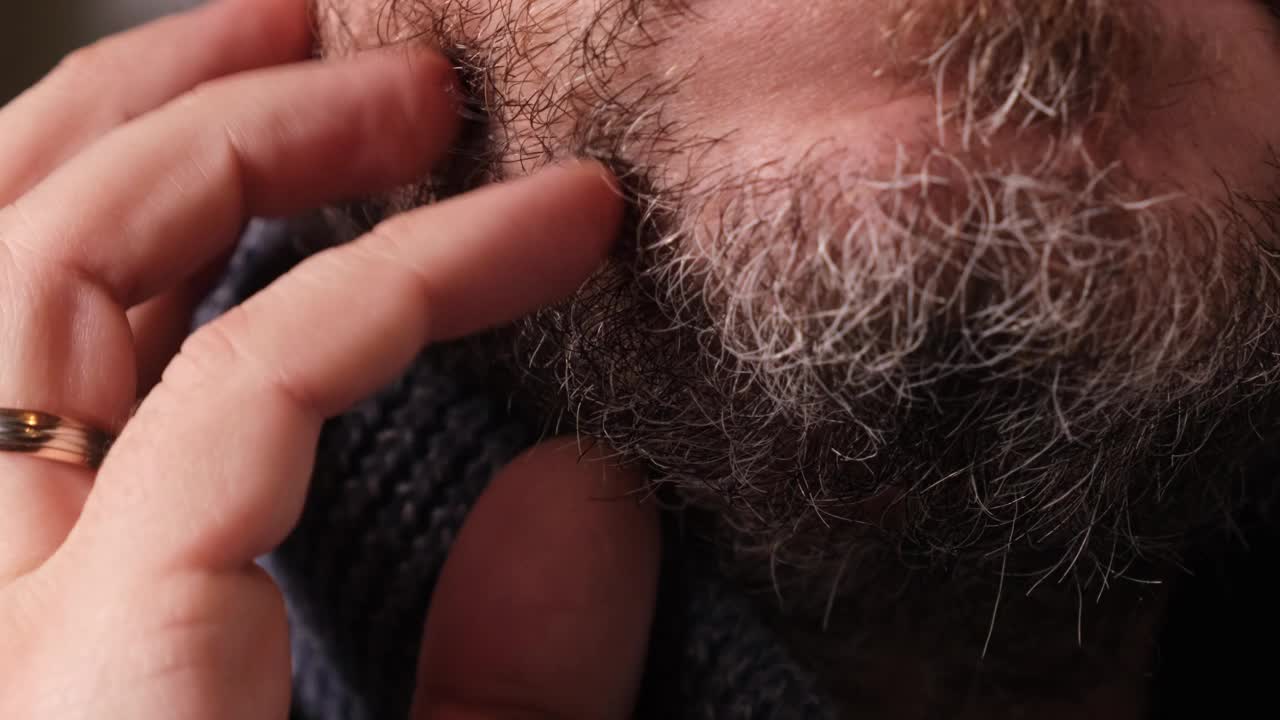 一个没刮胡子的男人抚摸着他的灰白胡须的特写镜头。视频素材