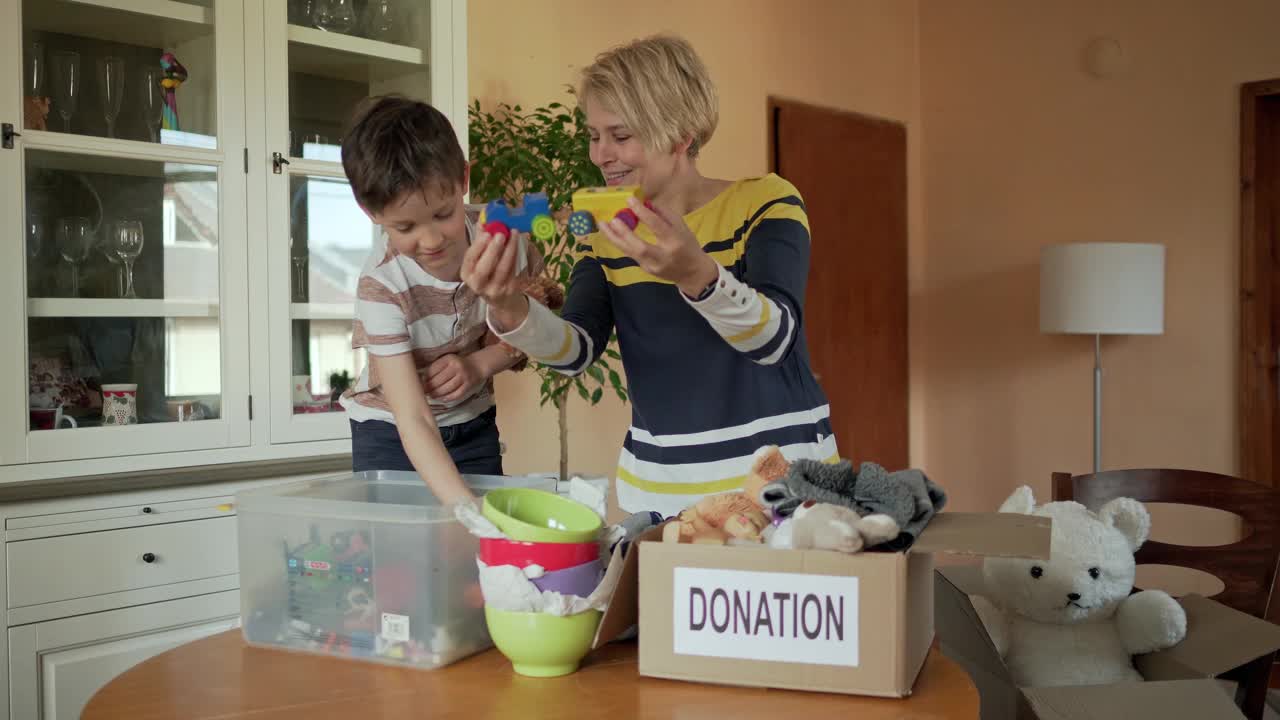 一个小男孩站在椅子上帮助他的母亲把慈善捐款和他想要的玩具分开视频素材