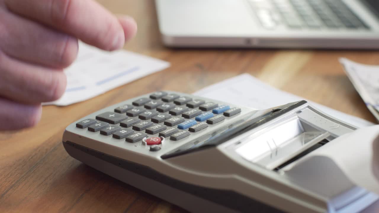 一个男人在家里用计算器算所得税的特写镜头。视频下载
