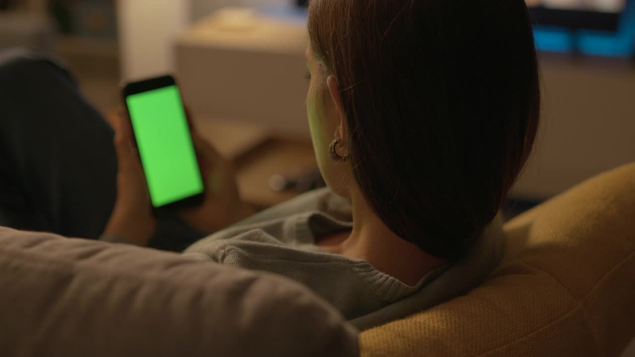 一位女士坐在沙发上用她的智能手机视频下载