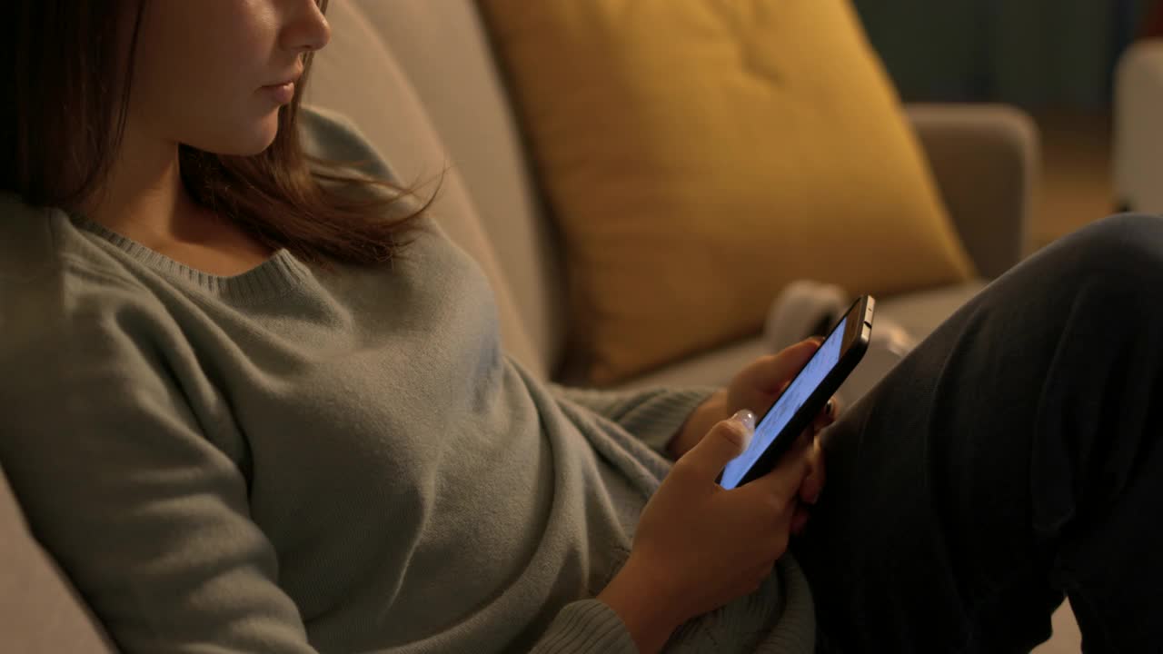 青春期的女孩坐在沙发上，用手机上网视频下载