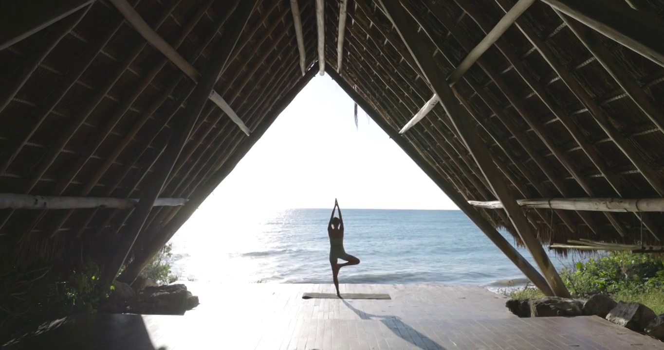 极端宽镜头的女人练习瑜伽在海洋前面的亭子在热带度假胜地视频素材