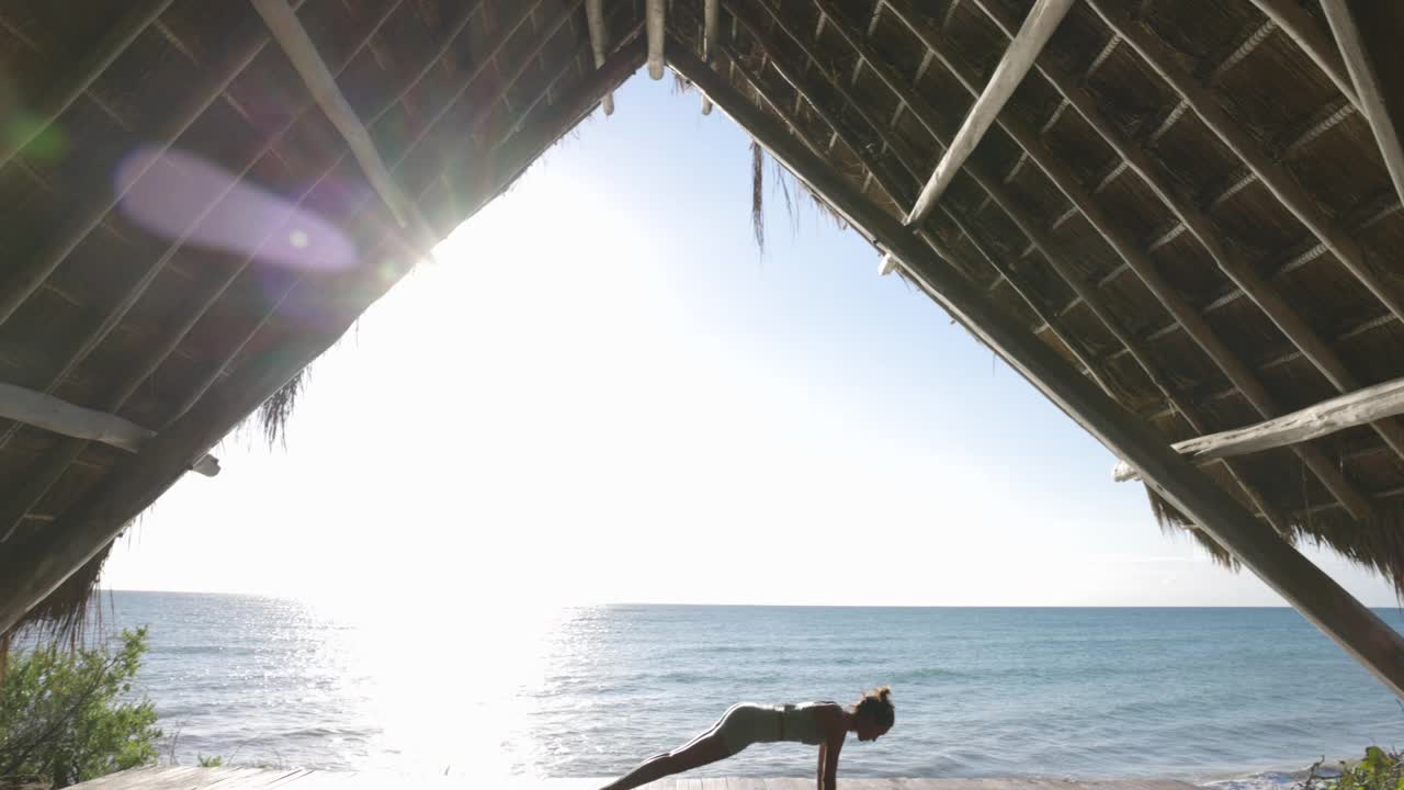 宽镜头的女人练习瑜伽在海洋前面的凉亭在热带度假村视频素材