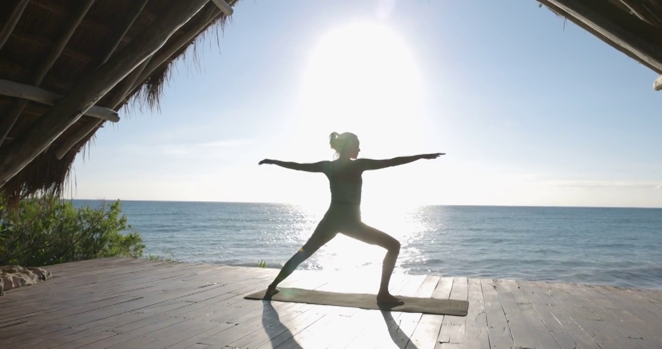 在热带度假胜地的海滨凉亭练习瑜伽的妇女宽镜头低角度视频素材