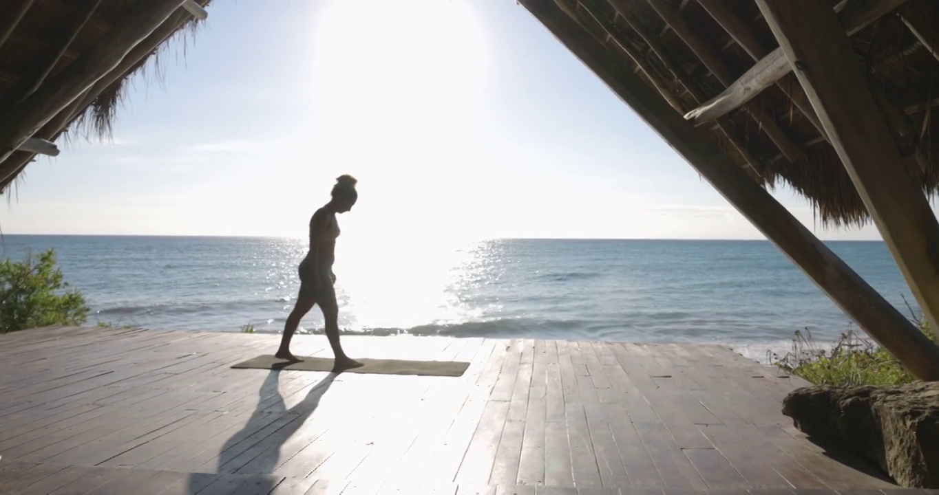 宽镜头的妇女练习瑜伽在海滨亭在热带度假视频素材