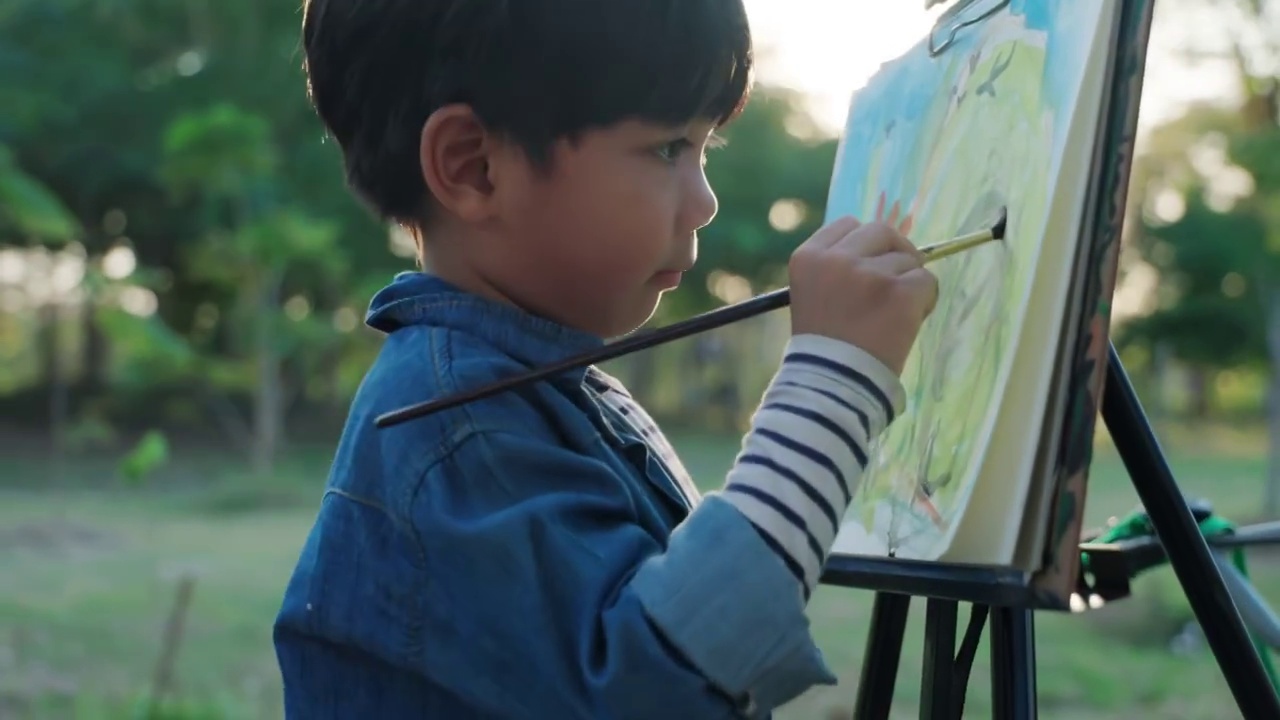 这个男孩用水彩画和画笔在村庄、公园里画画。视频下载