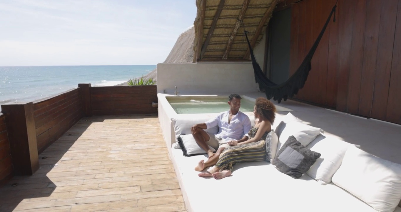 一对夫妇在俯瞰海洋的豪华热带别墅甲板上放松的广角镜头视频素材