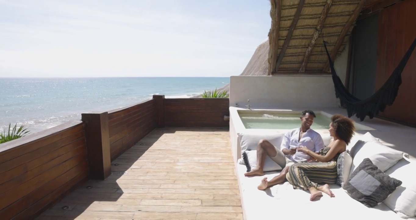 一对夫妇在俯瞰海洋的豪华热带别墅甲板上放松的广角镜头视频素材