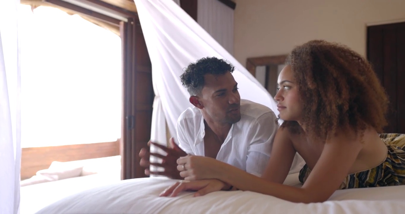 在热带度假胜地的豪华套房里，一对微笑的夫妇躺在床上放松视频素材