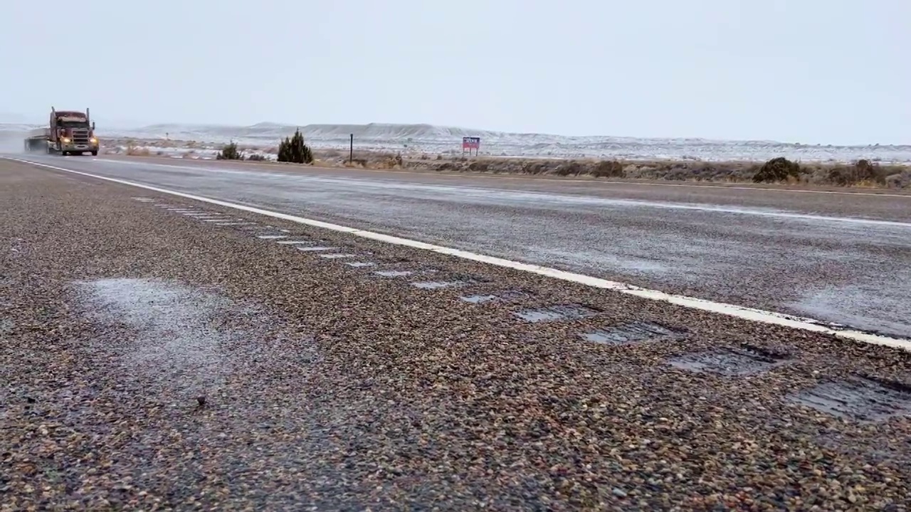 在下雪的时候，平板半挂车在潮湿的路面上穿越犹他州边境视频素材