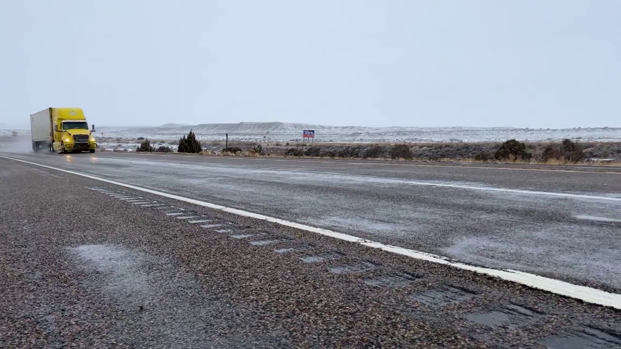 黄色的半卡车在下雪时行驶在潮湿的道路上穿越犹他州边境视频素材