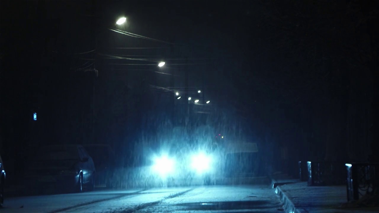 车灯开在铺有路面的街道上，外面正在下雪，虽然雪花很小视频下载