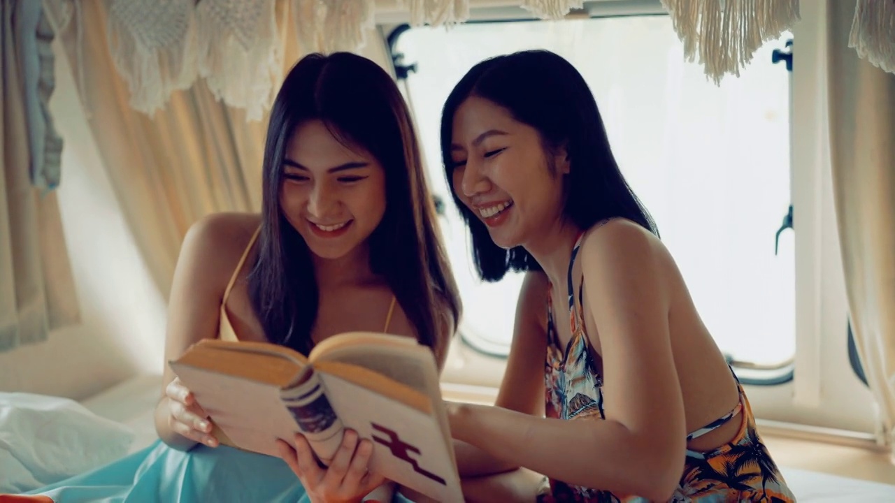 兄弟姐妹亚洲妇女读一本书一起在露营车。视频下载