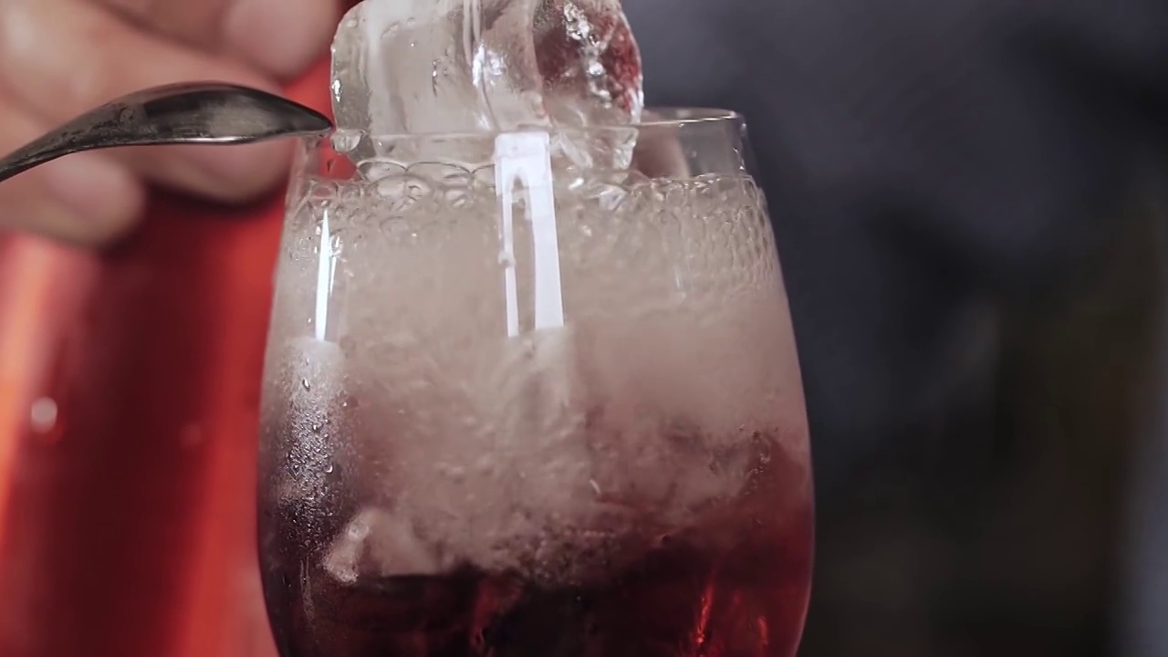 向装有冰块和红色糖浆的玻璃杯中加入苏打水。特写镜头视频下载