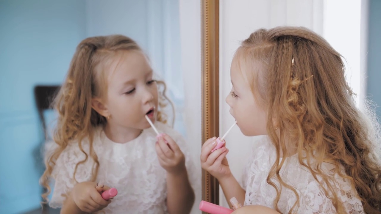 孩子画的嘴唇。肖像。可爱的卷发金发小女孩在镜子前用口红涂嘴唇视频素材