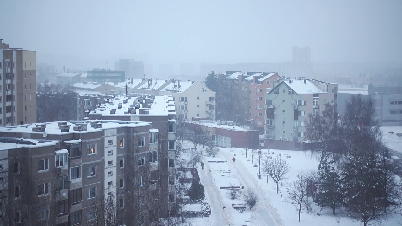 在冬天下雪的时候，从多层建筑的窗户看到城市。下雪天阴天，人在外面。4 k视频视频素材