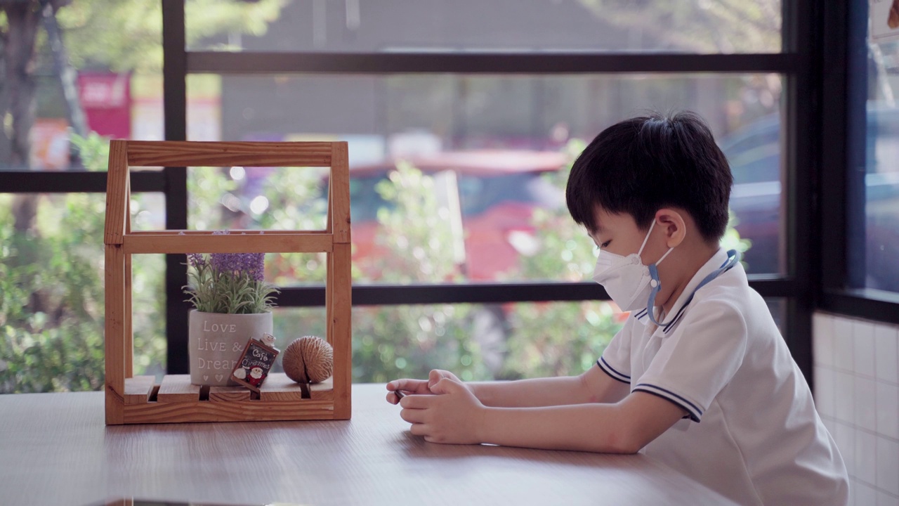 亚洲男孩独自在咖啡馆在线学习。儿子在智能手机上玩游戏。视频素材