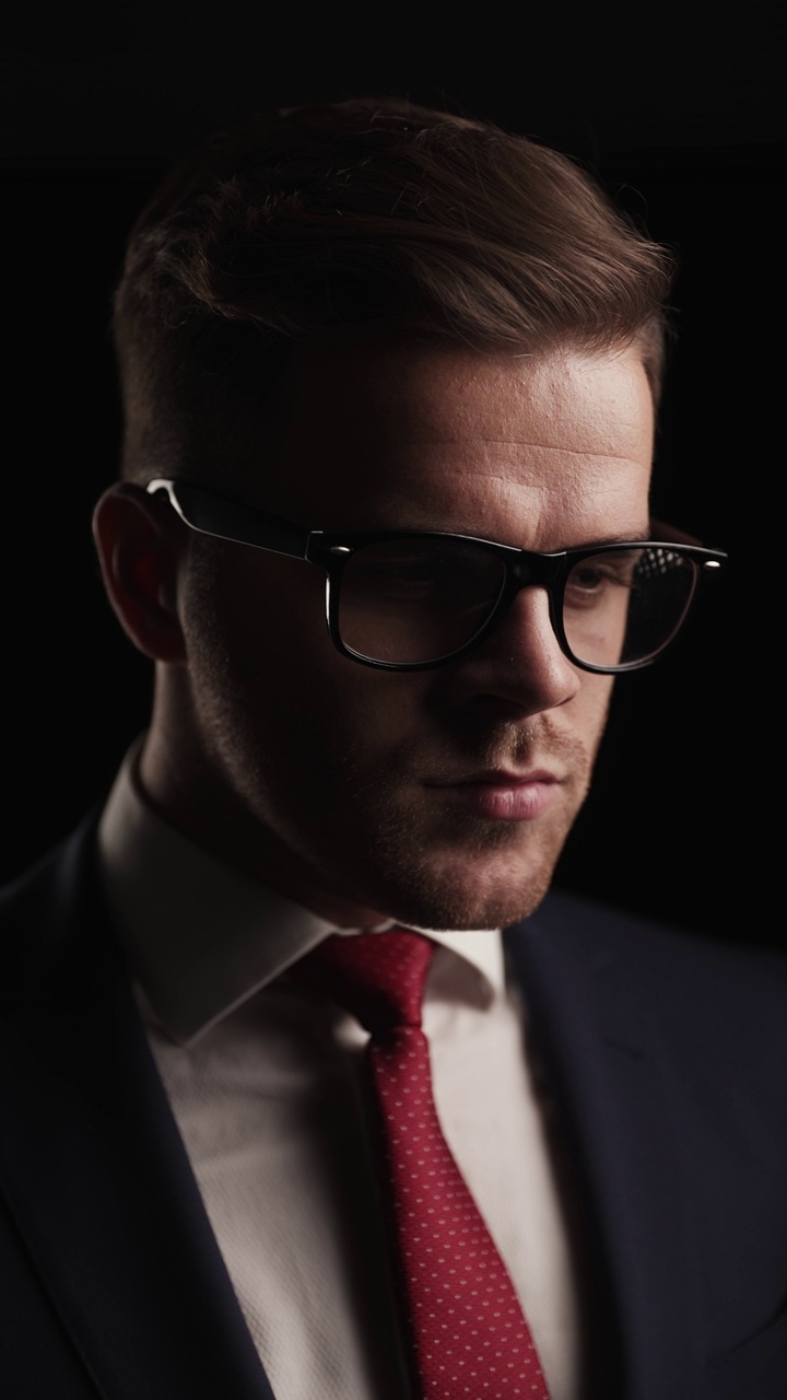 项目视频考虑周到的年轻商人，眼镜调整领带，看着一边，在黑暗中走在自信的态度视频下载