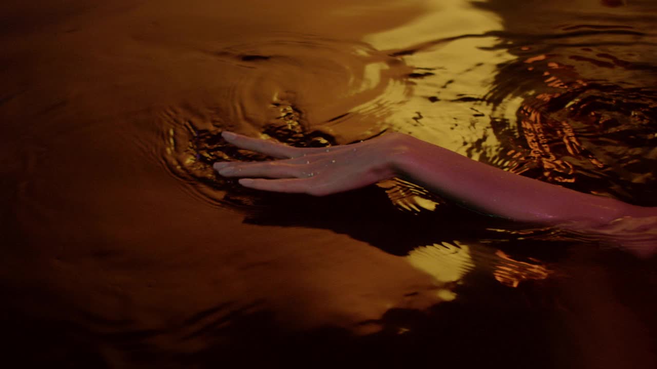 金色的，光滑的水面。女性用手轻轻泼洒并触摸液体视频素材