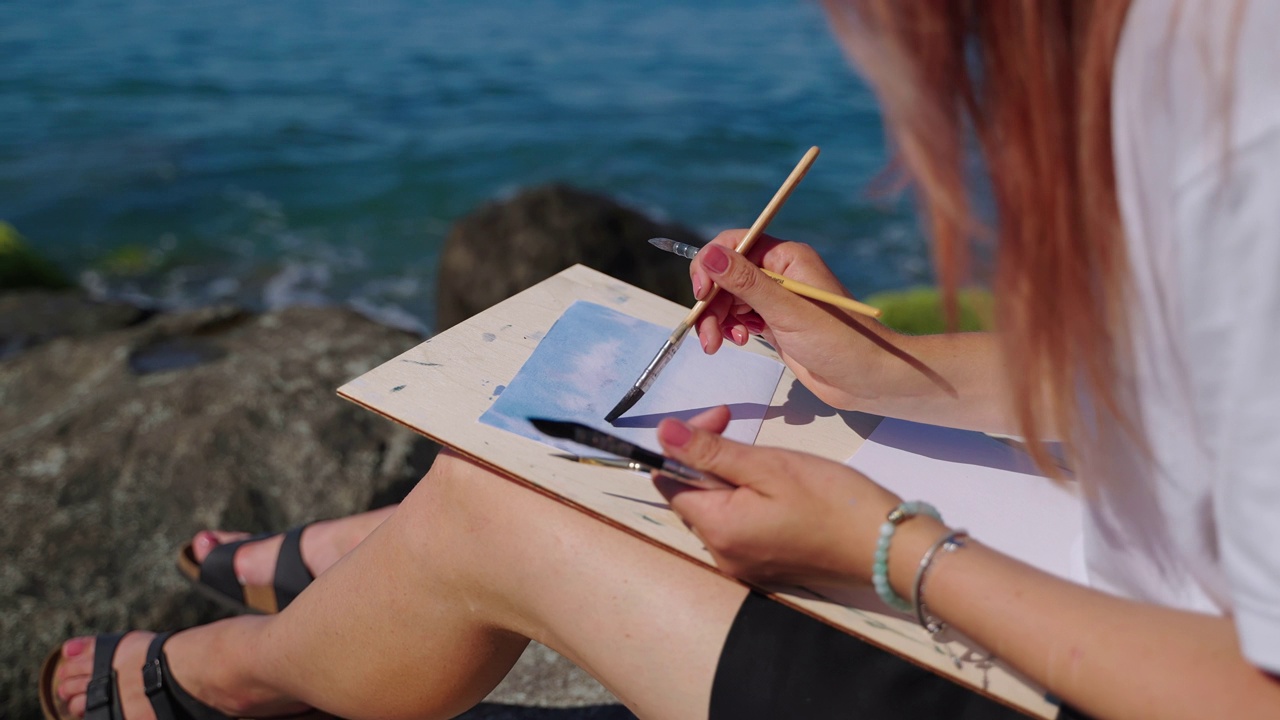美术学院的女学生坐在海边画着海洋风景视频素材