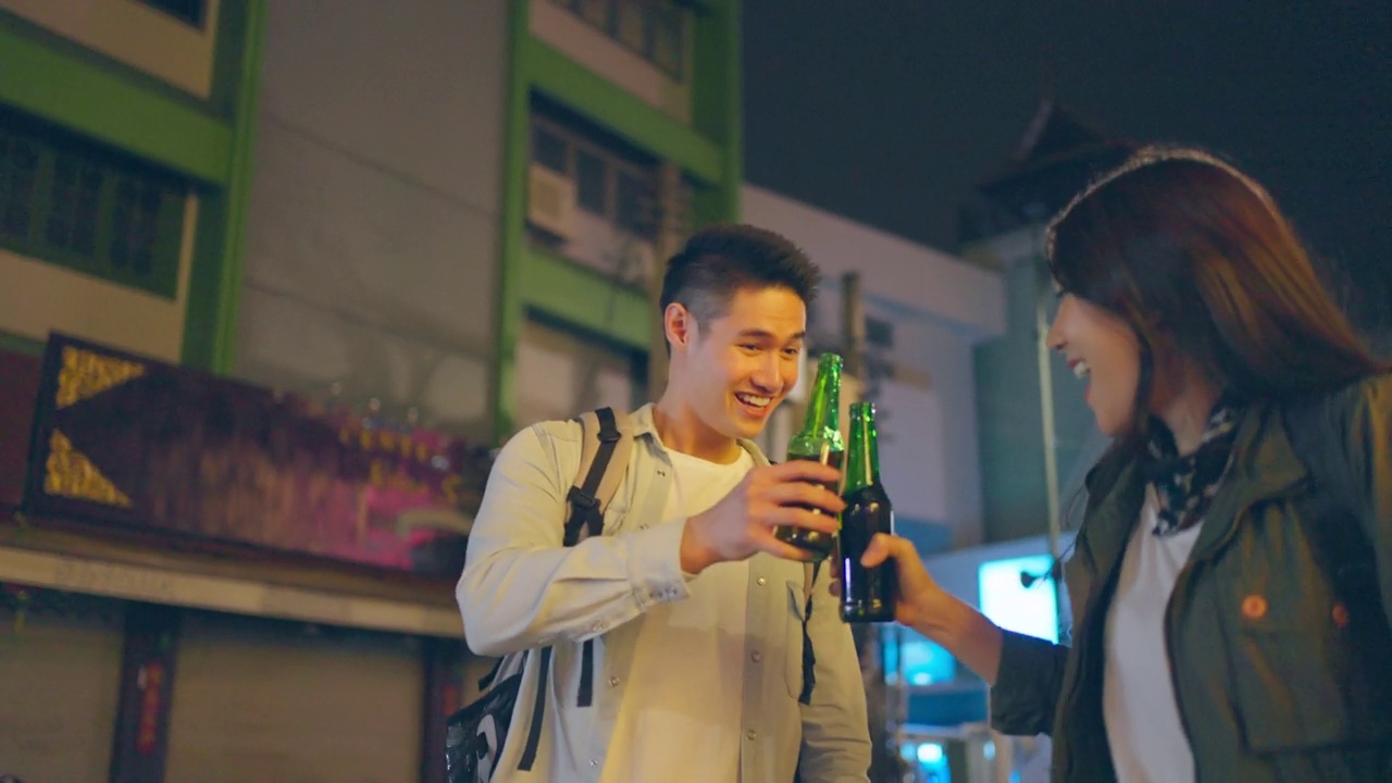 亚洲帅哥情侣一起喝酒开派对。在城市里旅游的青年男女，在假期里一起拿着一瓶啤酒，在漆黑的夜晚在路上度过时光。视频素材