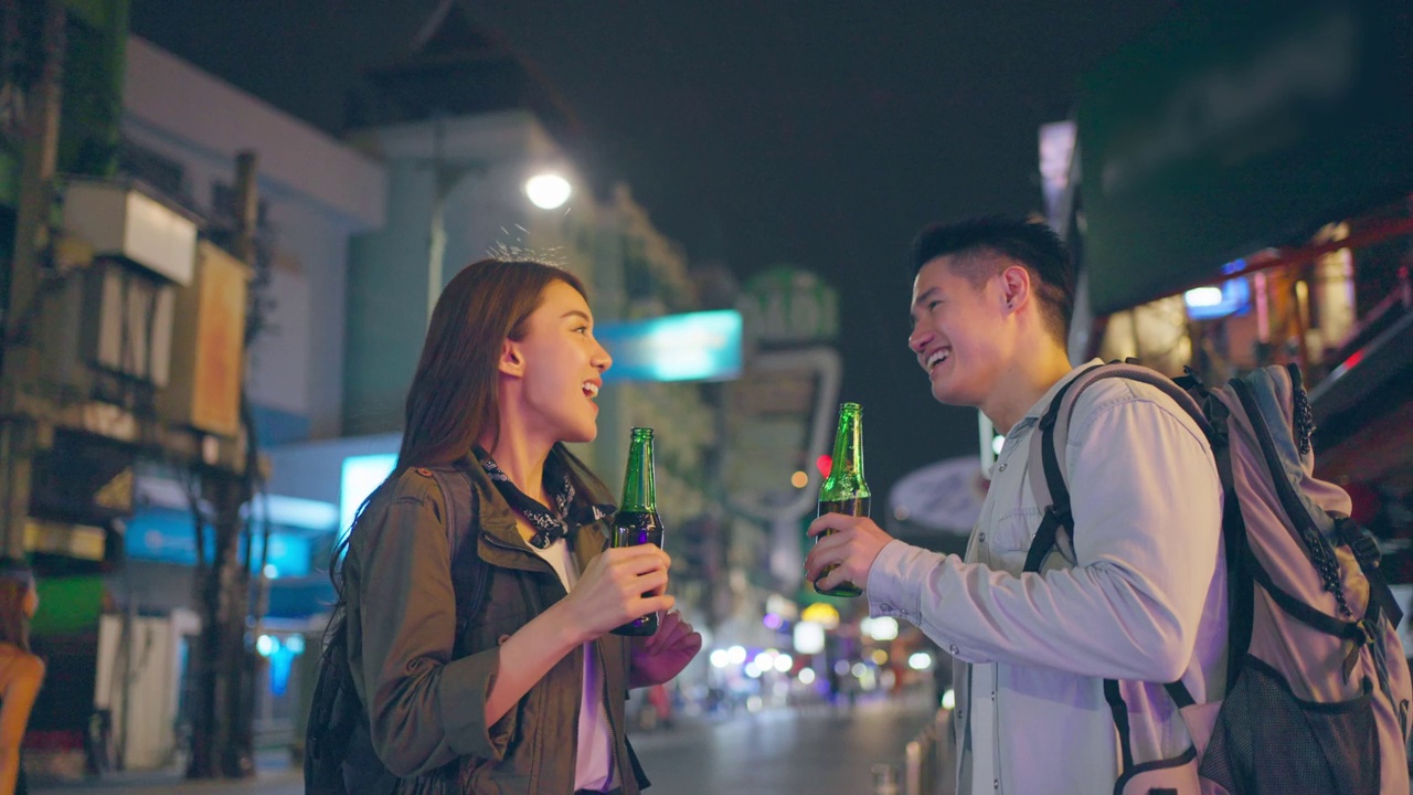 亚洲帅哥情侣一起喝酒开派对。在城市里旅游的青年男女，在假期里一起拿着一瓶啤酒，在漆黑的夜晚在路上度过时光。视频素材