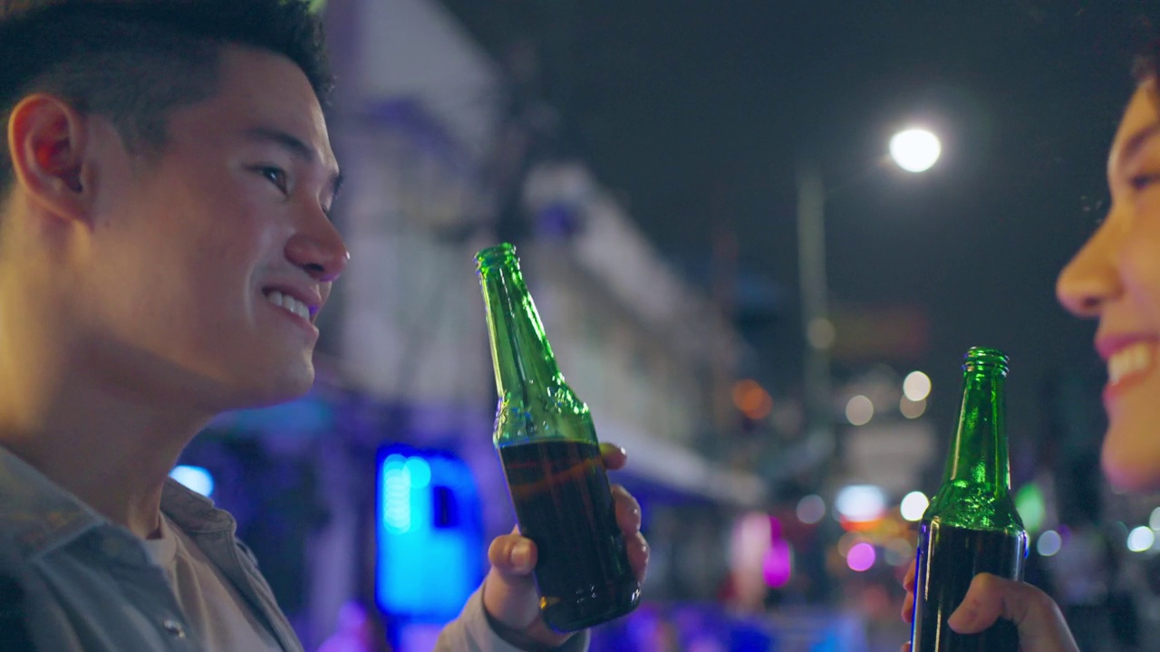 亚洲帅哥情侣一起喝酒开派对。在城市旅游的年轻男女在假期的夜晚一起在路上碰碰啤酒视频素材