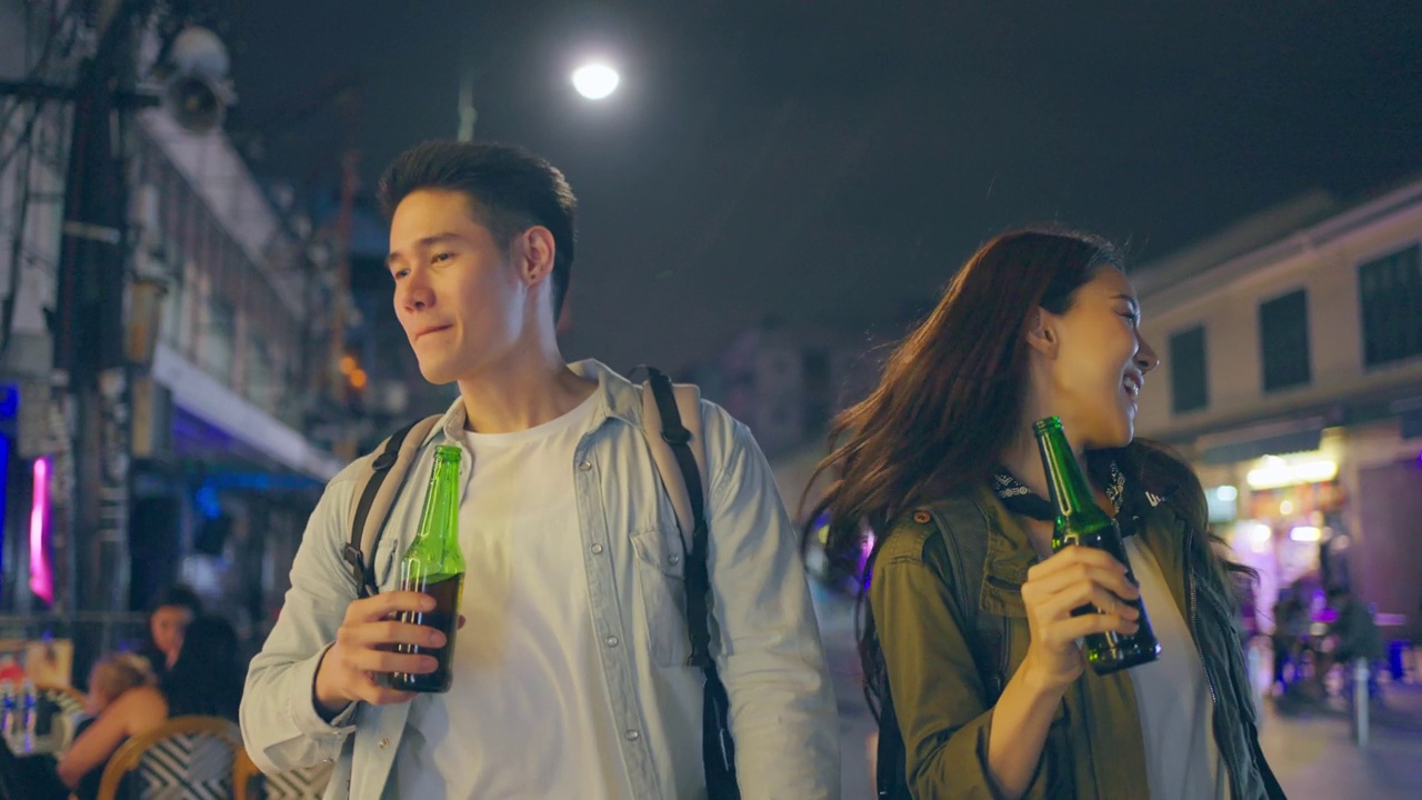 亚洲帅哥情侣一起喝酒开派对。在城市里旅游的青年男女，在假期里一起拿着一瓶啤酒，在漆黑的夜晚在路上度过时光。视频下载