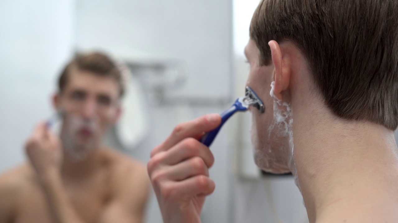 一个男人的后脑勺的特写镜头，在淋浴后刮他的脸，一个千年老人在打理他的胡茬或胡子，在早晨洗澡时做面部美容手术，视频素材