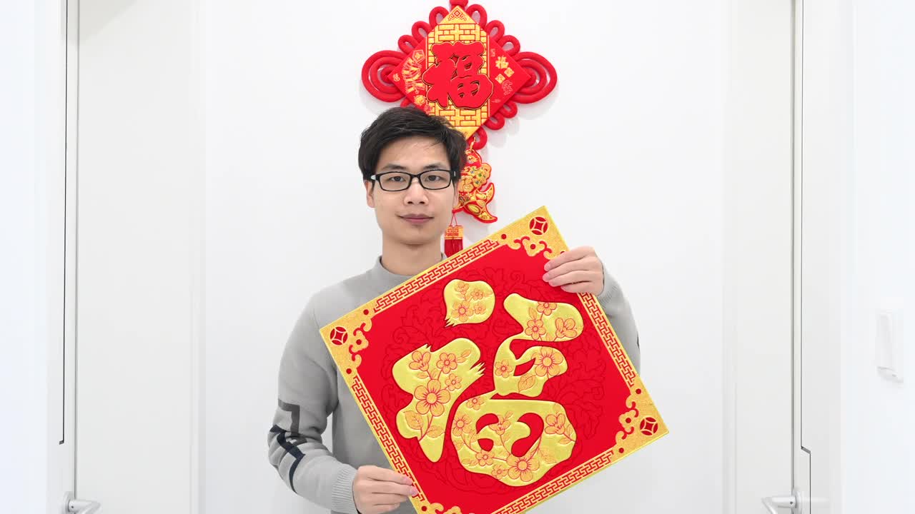 一位年轻的亚洲成年男性拿着写有“福”字的春联，微笑着向镜头展示视频下载