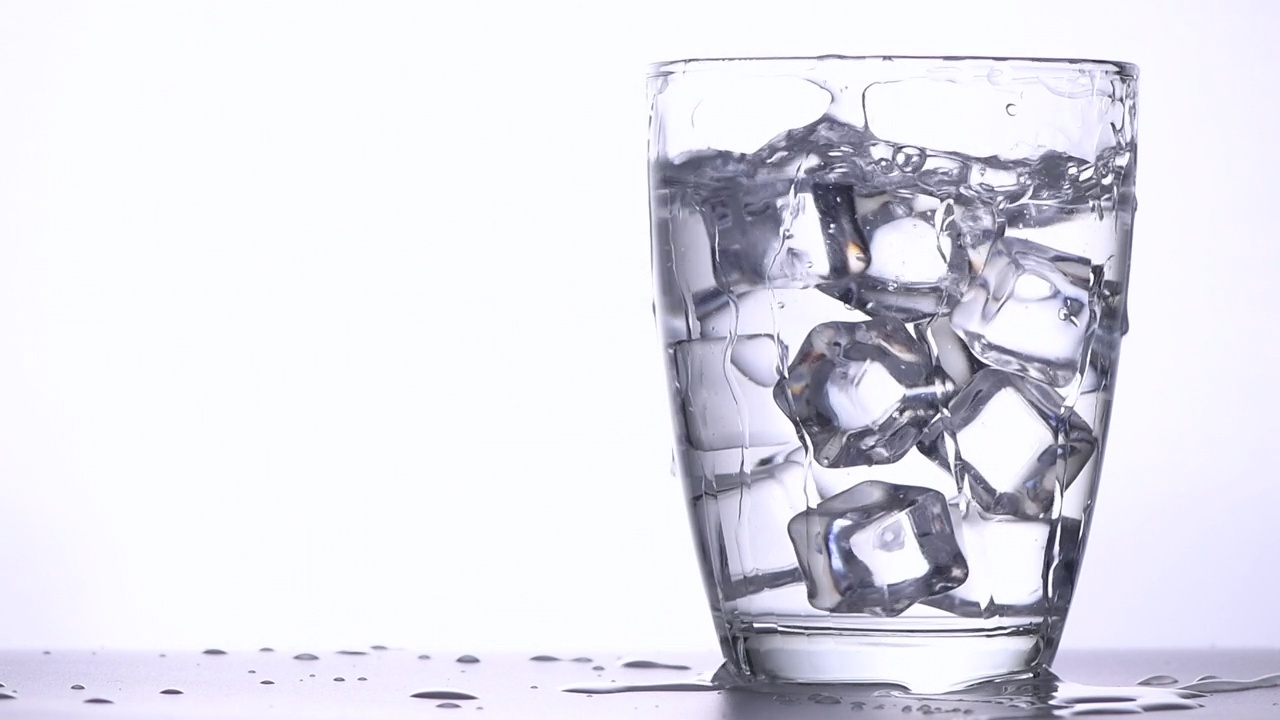 冰块掉落到有清水或酒精的玻璃杯中，溅起水花并在杯中旋转。视频素材