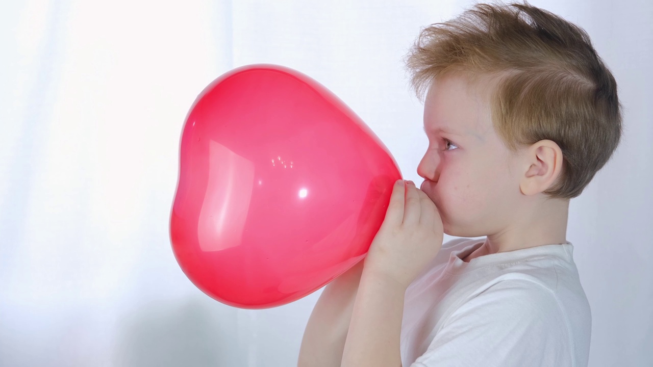 情人节,孩子。可爱的小男孩在情人节或母亲节在白色的背景上吹一个心形的气球。视频下载