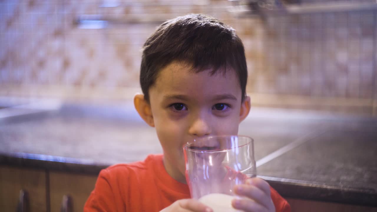 黑发小男孩喝着杯子里的牛奶，舔着嘴唇视频素材