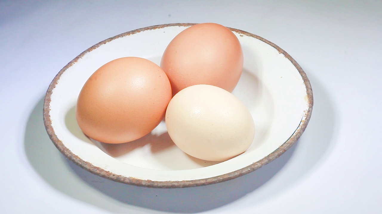 生鸡肉，棕色和白色混合鸡蛋在一个盘子孤立的白色背景旋转360平稳运动。视频素材