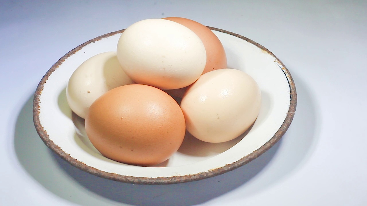 生鸡肉，棕色和白色混合鸡蛋在一个盘子孤立的白色背景旋转360平稳运动。视频素材
